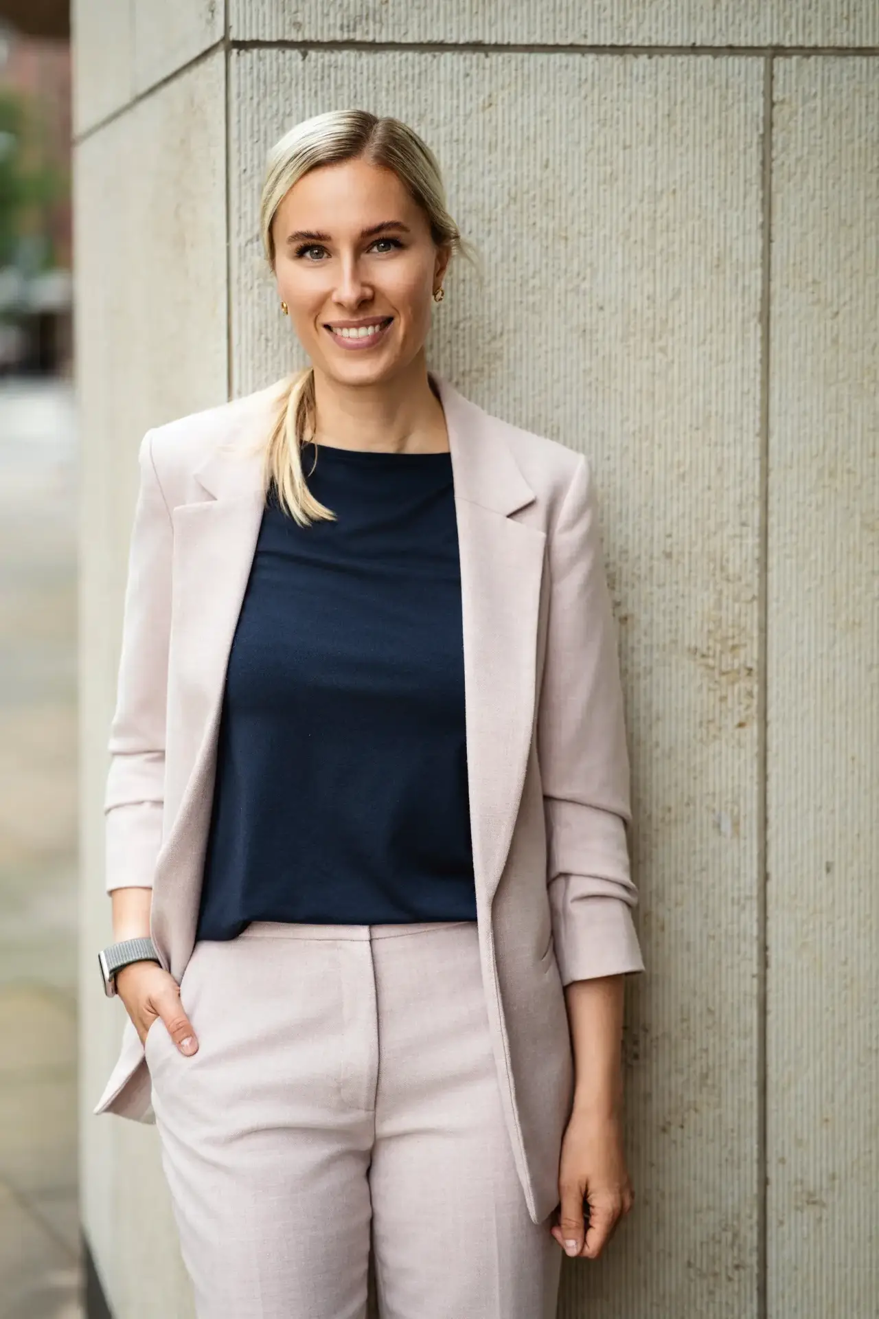 Businessportrait einer blonden Frau im hellen Hosenanzug als Außenaufnahme an einer Steinwand in Hamburg