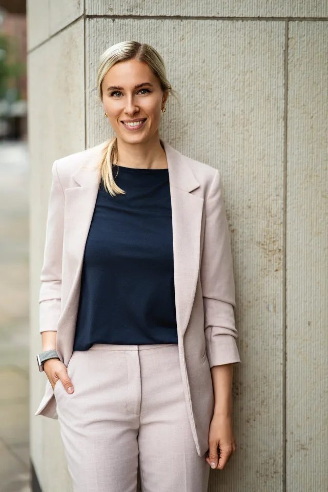 Businessportrait einer blonden Geschäftsfrau im rosa Blazer vor Sandsteinwand in Hamburg