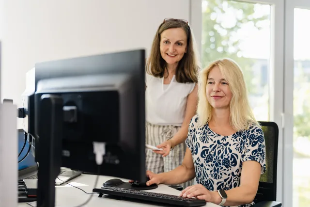 Mitarbeiterfotos Hamburg – zwei Kolleginnen lächeln gemeinsam am Arbeitsplatz im hellen Büro für authentisches Employer Branding