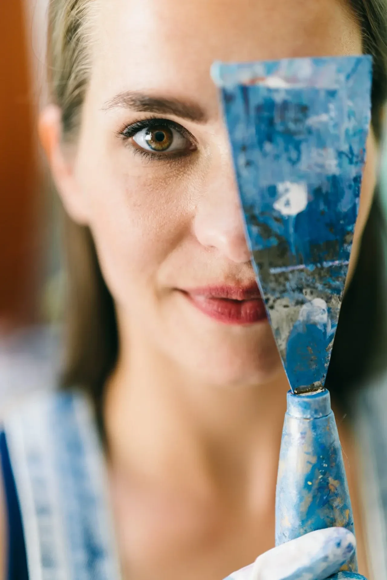 Künstlerportrait einer Malerin, die eine blau bemalte Spachtel vor ihr Gesicht hält – Atelier in Hamburg