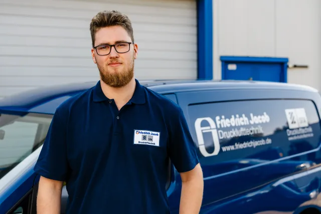 Mitarbeiterfoto Techniker vor blauem Servicefahrzeug, gleicher Bildausschnitt